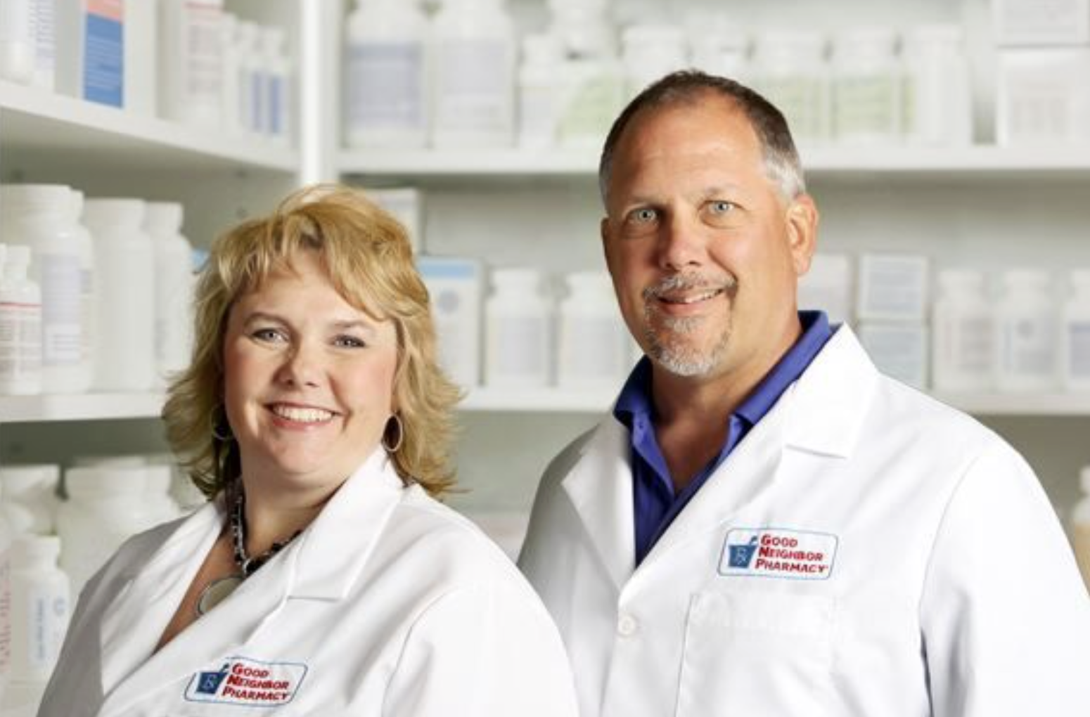 Two smiling Family Pharmacy of Pottsboro pharmacists in white coats standing in front of shelves of medications