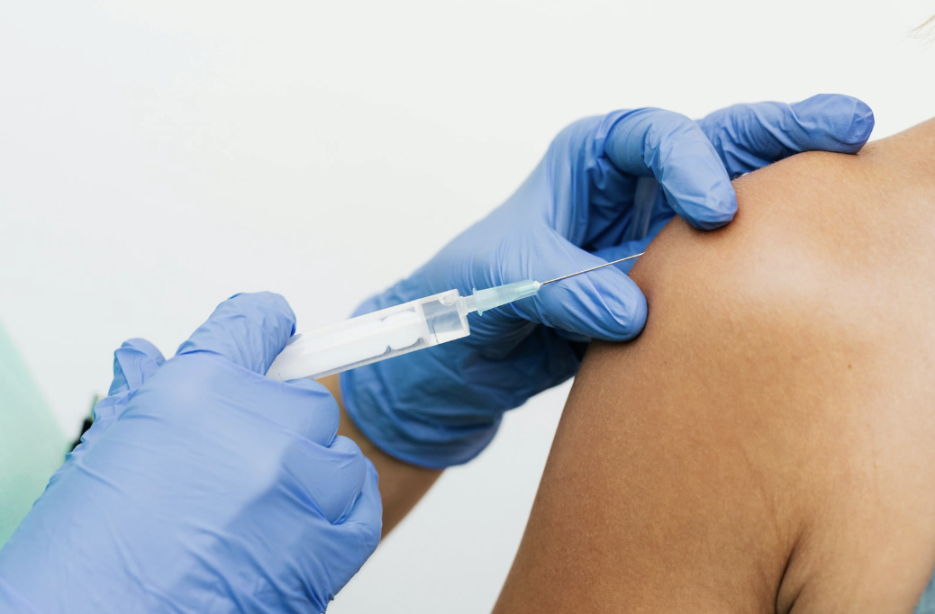 A gloved pharmacist administering a vaccine injection into a patient’s upper arm
