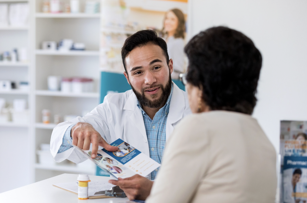 A pharmacist going over a medication information sheet with a patient at the pharmacy counter